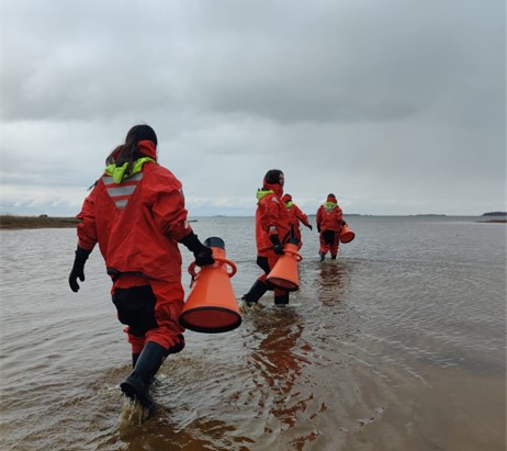 People wading out into the water wearing red survival suits